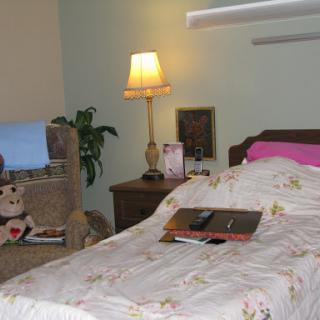 A cozy bedroom setup featuring a bed with floral bedding, a bedside lamp, and a comfortable chair.