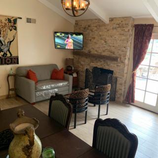 A cozy living room featuring a stone fireplace, wall-mounted TV, and dining area with chairs.
