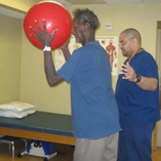 A person engaging in a physical therapy session with an instructor using an exercise ball.