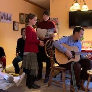 A family gathering where one person plays guitar while others sing along in the living room.