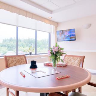 A bright and inviting interior space featuring a circular table, comfortable chairs, a floral centerpiece, and a large window with a view.