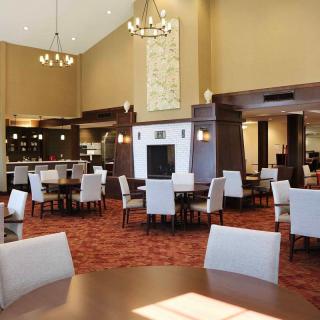 A spacious dining area with neatly arranged tables and chairs, adorned with chandeliers and a central fireplace.