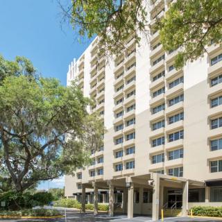 A high-rise apartment building with surrounding trees under a clear blue sky.