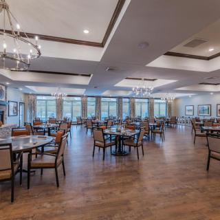 A spacious dining room with elegant chandeliers, wooden flooring, and neatly arranged tables and chairs.