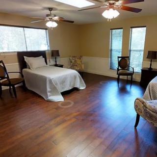 Spacious bedroom with wooden floors, featuring a single bed, multiple chairs, and ceiling fans.