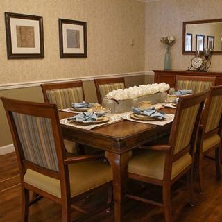 A dining room with a wooden table and chairs, elegantly set for a meal, featuring framed art on the walls.