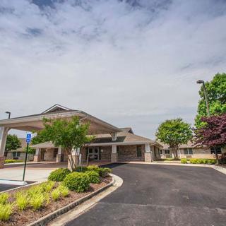 A modern building with a circular driveway and well-maintained landscaping under a partly cloudy sky.