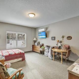A cozy bedroom with a bed, chairs, and a wall-mounted television.
