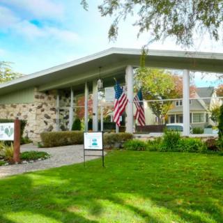 A modern building with a stone facade and flags displayed outside, set against a lush green lawn and trees.