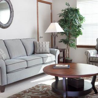 A cozy living room with a grey sofa, round wooden coffee table, and a floor lamp next to a potted plant.