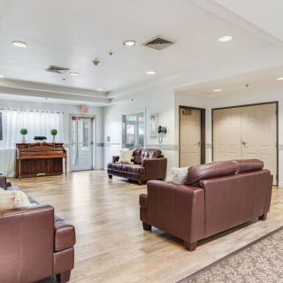 A spacious living area featuring leather sofas and a piano, with modern decor and wood flooring.