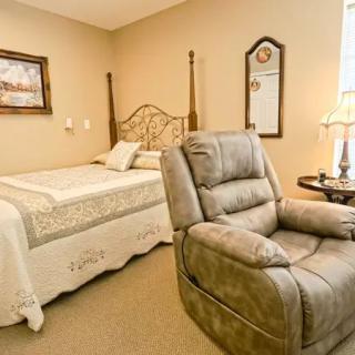 A cozy bedroom featuring a bed, reclining chair, and decorative elements like a mirror and lamp.