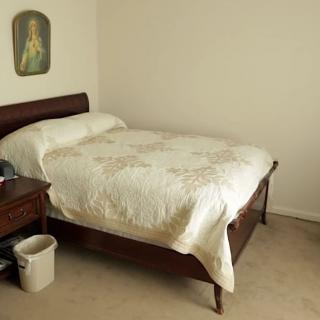 A simple bedroom with a neatly made bed, nightstand, and artwork on the wall.