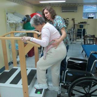 A therapist assists an elderly woman with rehabilitation exercises on a set of training stairs.