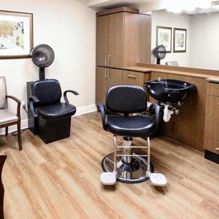 A modern hair salon interior with styling and dryer chairs, a sink, and wooden cabinets.