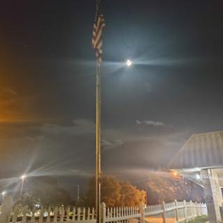 A night scene featuring a flag pole illuminated by artificial lights and the moon in the background.