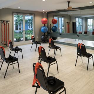 A spacious exercise room with chairs arranged for a workout session, featuring mirrors and fitness equipment.