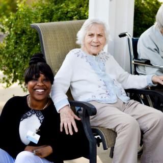 A caregiver sitting with elderly individuals outdoors, enjoying a sunny day.