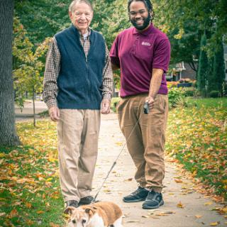 Two individuals enjoying a stroll with a dog on a picturesque autumn day.