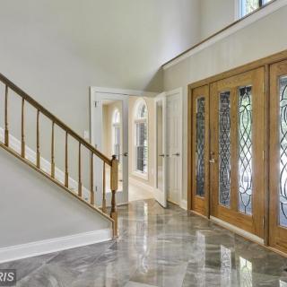 A spacious entryway with a polished floor and wooden staircase, featuring decorative glass doors.
