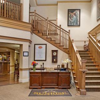 A hotel lobby with a wooden reception desk, decorative staircase, and framed artwork on the walls.