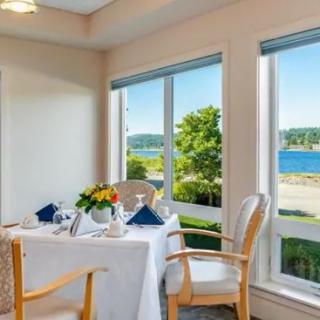 A cozy dining area with a beautifully set table, overlooking a scenic waterfront through large windows.