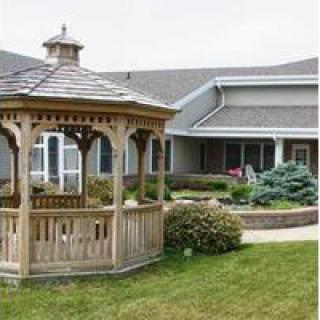 A wooden gazebo in a landscaped yard next to a house.