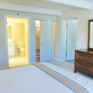 A bright bedroom with a view into an adjacent bathroom, featuring a dresser and mirror.