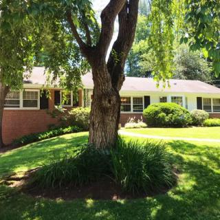 A charming house with a brick facade and lush front yard featuring a large tree.