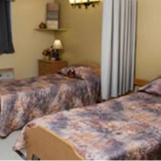 A cozy bedroom with two twin beds featuring patterned bedding, a bedside table with a lamp, and a shelf on the wall.