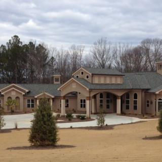 A large brick residential house with landscaped surroundings and a cloudy sky.