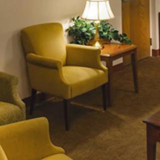 A cozy living room area featuring yellow armchairs, a lamp on a wooden side table, and a carpeted floor.