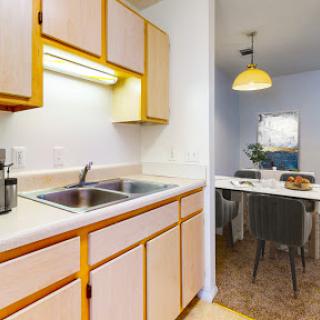 A cozy kitchen with wooden cabinets, equipped with a sink and adjacent dining area.