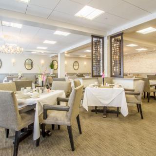 An elegant restaurant dining area with neatly arranged tables and chairs, adorned with white tablecloths and a chandelier.