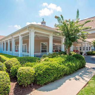 A well-maintained building with a large porch surrounded by lush green landscaping on a sunny day.
