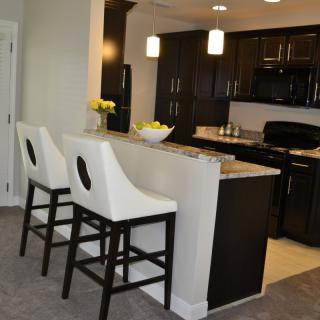 A modern kitchen with dark cabinets and a breakfast bar featuring stylish white bar stools.