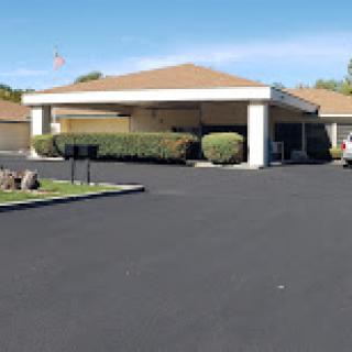 A well-maintained single-story building with a paved driveway and neatly trimmed bushes.