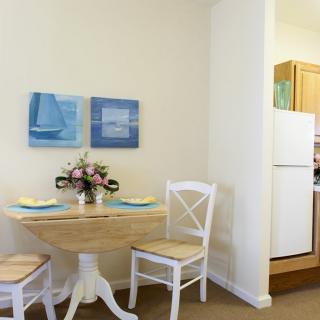 A cozy dining area with a small table, two chairs, and floral centerpiece near a kitchen.