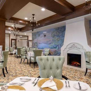 A cozy and elegantly designed restaurant featuring comfortable green chairs, a warm fireplace, and artistic wall murals.