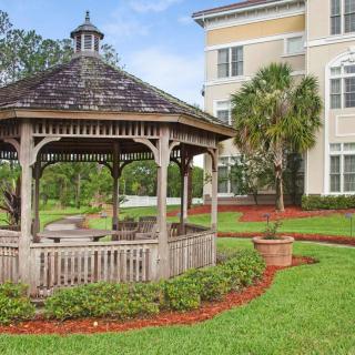 A wooden gazebo surrounded by a well-maintained garden with a nearby building.