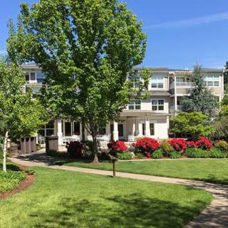 A scenic view of a residential building surrounded by lush greenery and vibrant flowers under a clear blue sky.