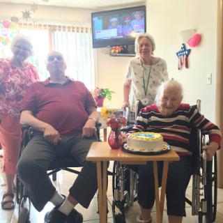 A joyful birthday celebration with family members gathered around an elderly woman in a wheelchair.
