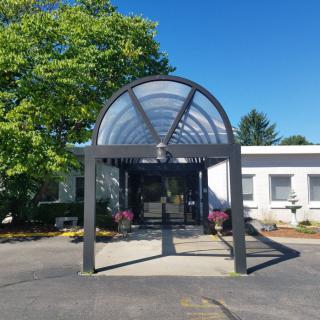 A building entrance with a transparent canopy under a clear blue sky.