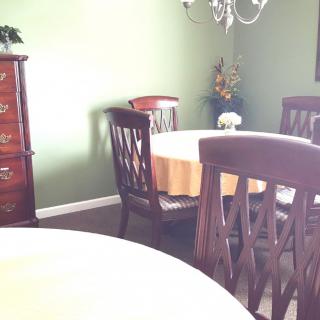 A cozy dining room with a round table, wooden chairs, and a chandelier.