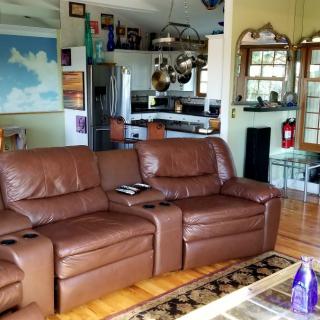 A cozy living room with a brown leather sofa and an open view of the kitchen area.