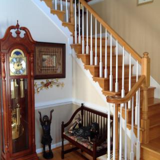 A home interior featuring a wooden staircase, a classic grandfather clock, and a decorative bench.