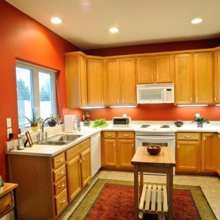 A modern kitchen with wooden cabinets and red walls, featuring a centered island and various appliances.