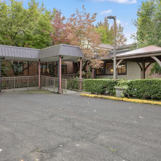 A view of a building with a covered entrance, surrounded by trees and foliage.