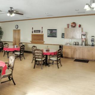 An empty dining area with round tables covered in red tablecloths, surrounded by chairs, and a coffee station along the wall.