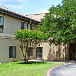 A two-story building surrounded by greenery with trees and a clear sky.